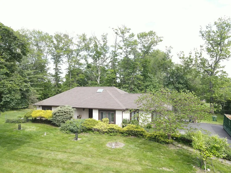 A suburban house nestled among trees on a grassy hill
