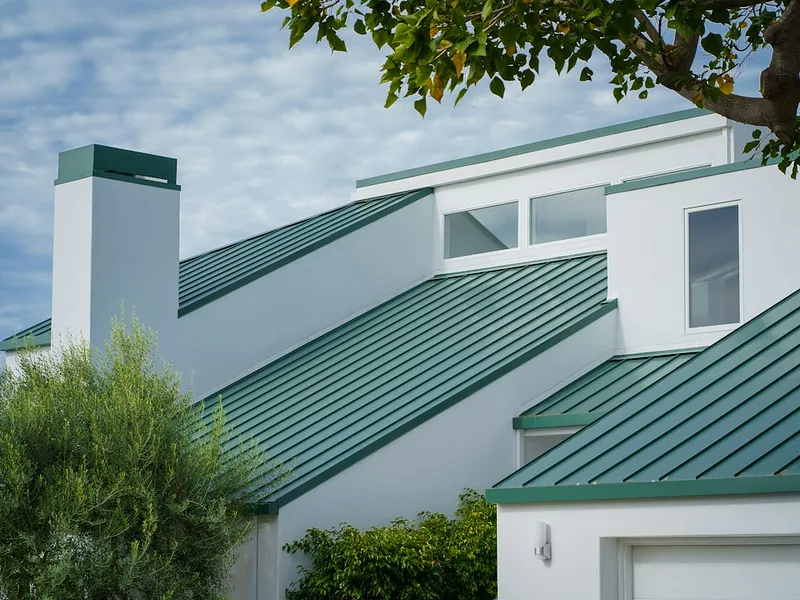 a white house with a green roof and a tree