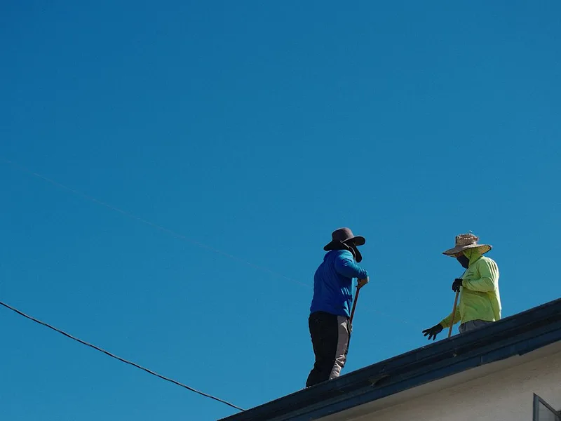 Two workers on a roof under a clear blue sky